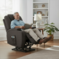 Man sitting in a gray recliner chair reading a book in a living room.